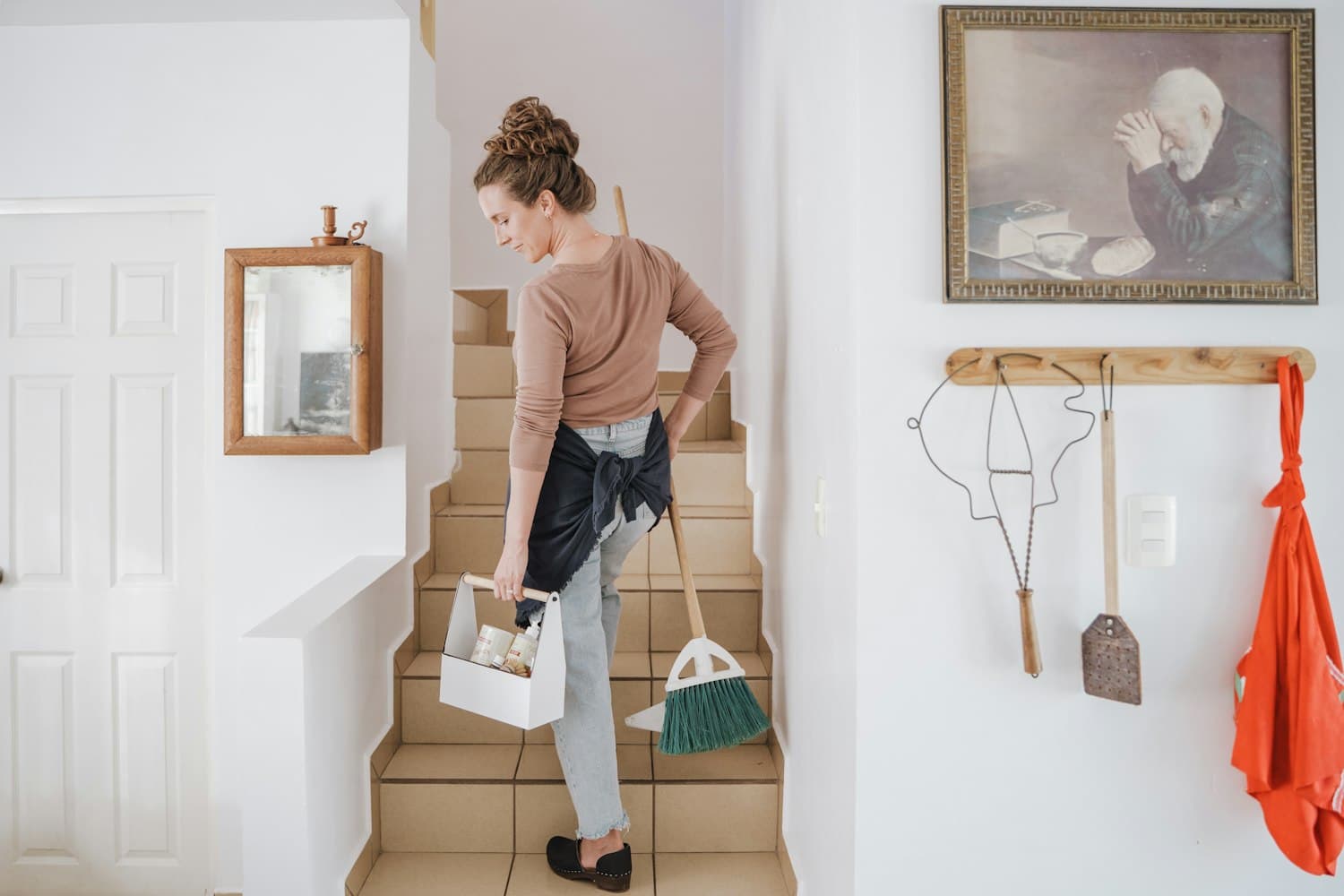 A professional cleaner carrying a cleaning caddy and broom up the stairs of a bright Melbourne home
