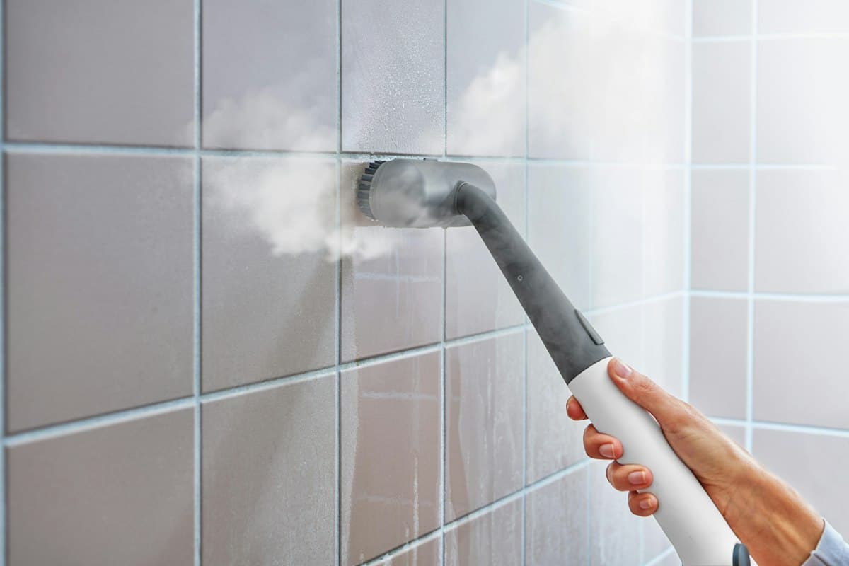 A steam cleaner lifting built-up grime from bathroom wall tiles and grout