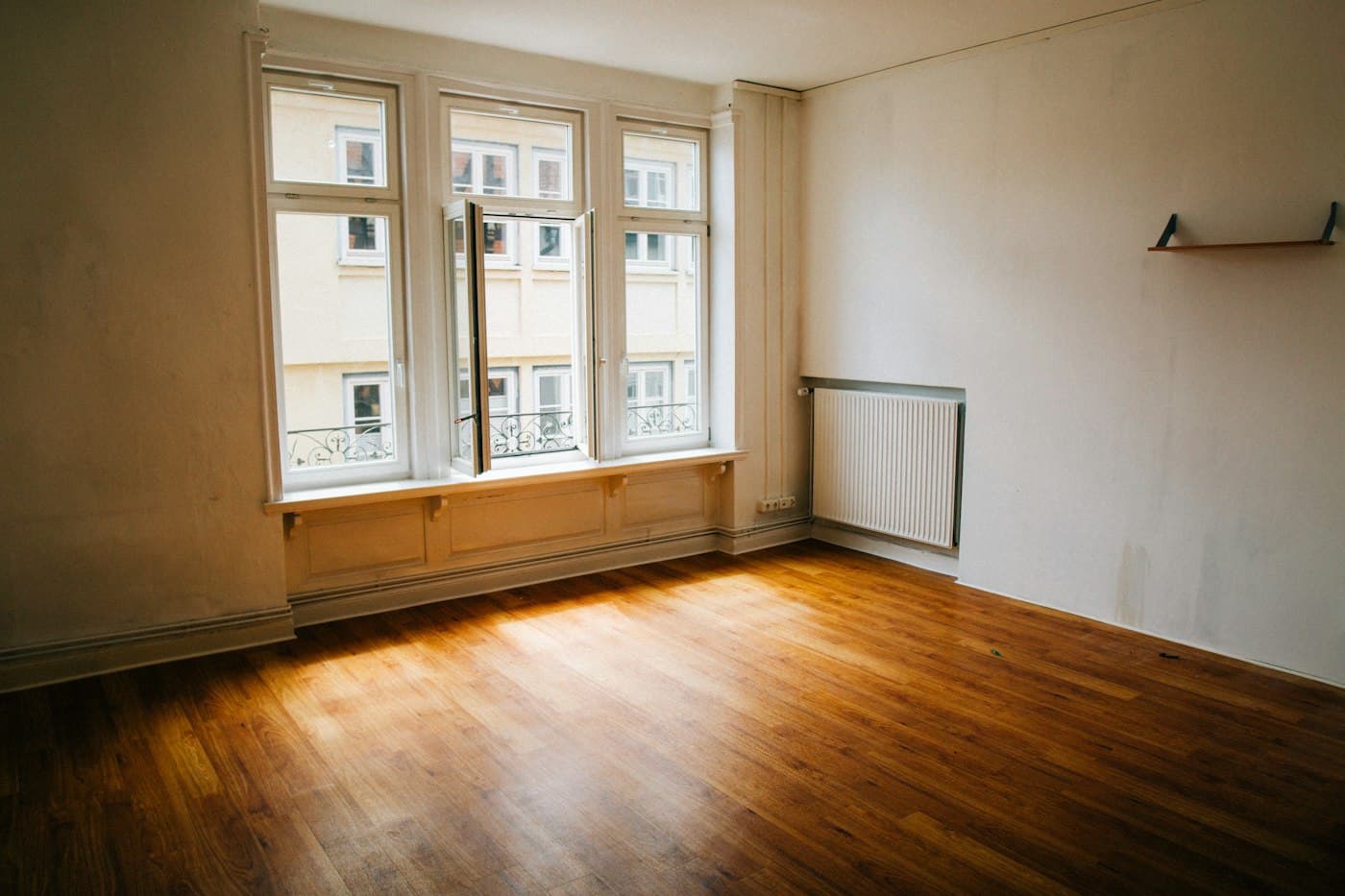 An empty apartment room with polished timber floors and sunlight through the window, ready for handover
