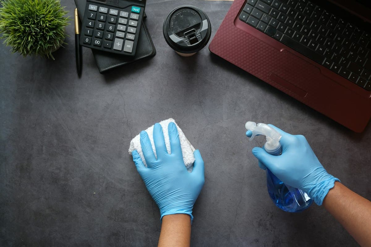 Gloved hands wiping down an office desk with cleaning spray and a cloth