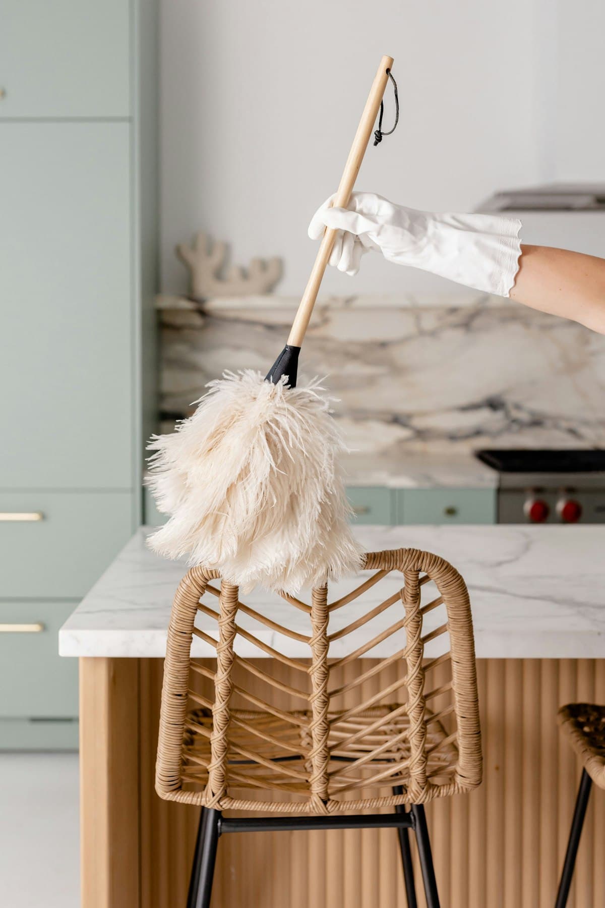 A gloved hand dusting a marble kitchen island with a soft-bristle duster
